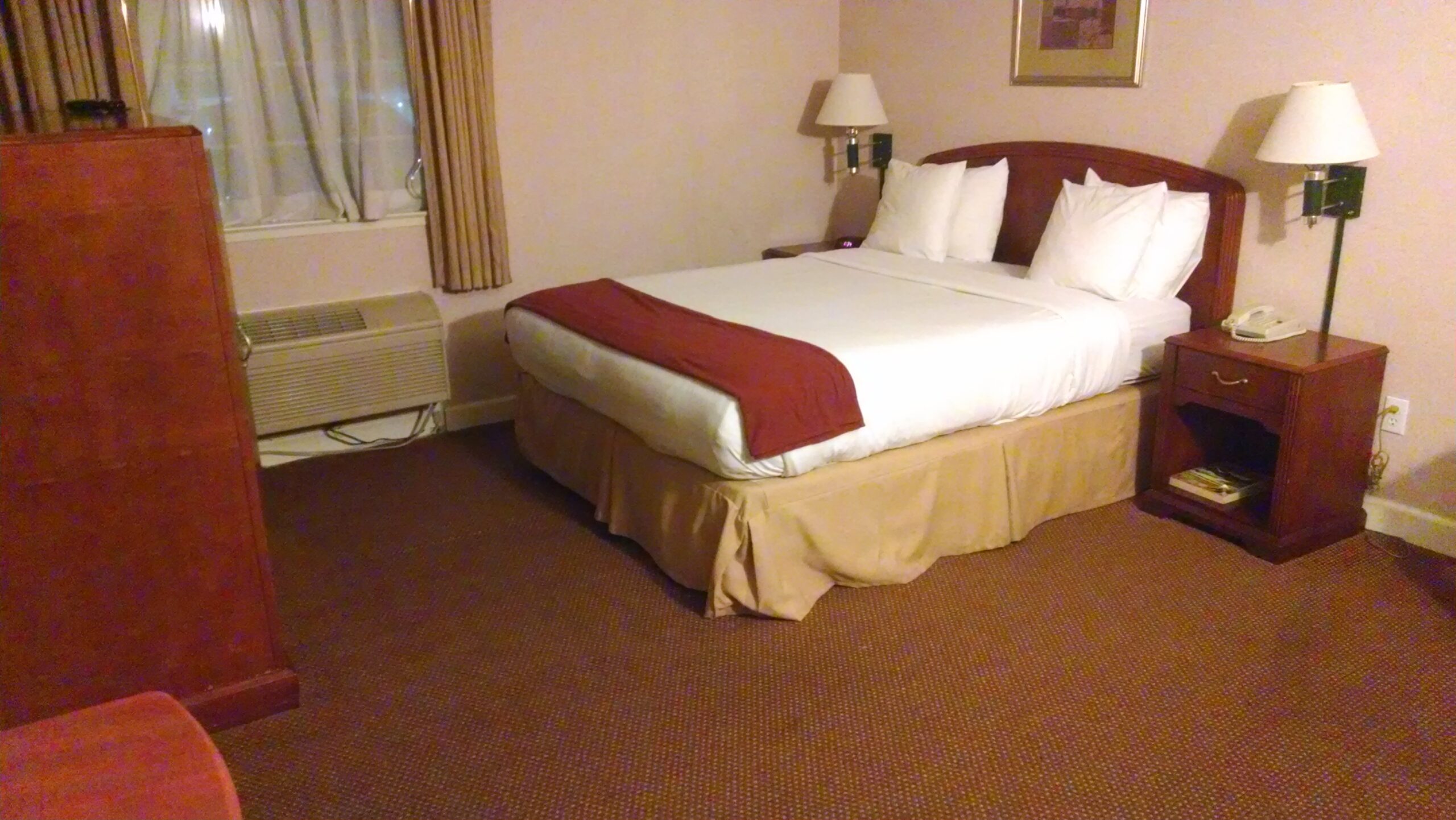 Queen-size hotel bed with white pillows, bedside tables, wall lamps and a window.
