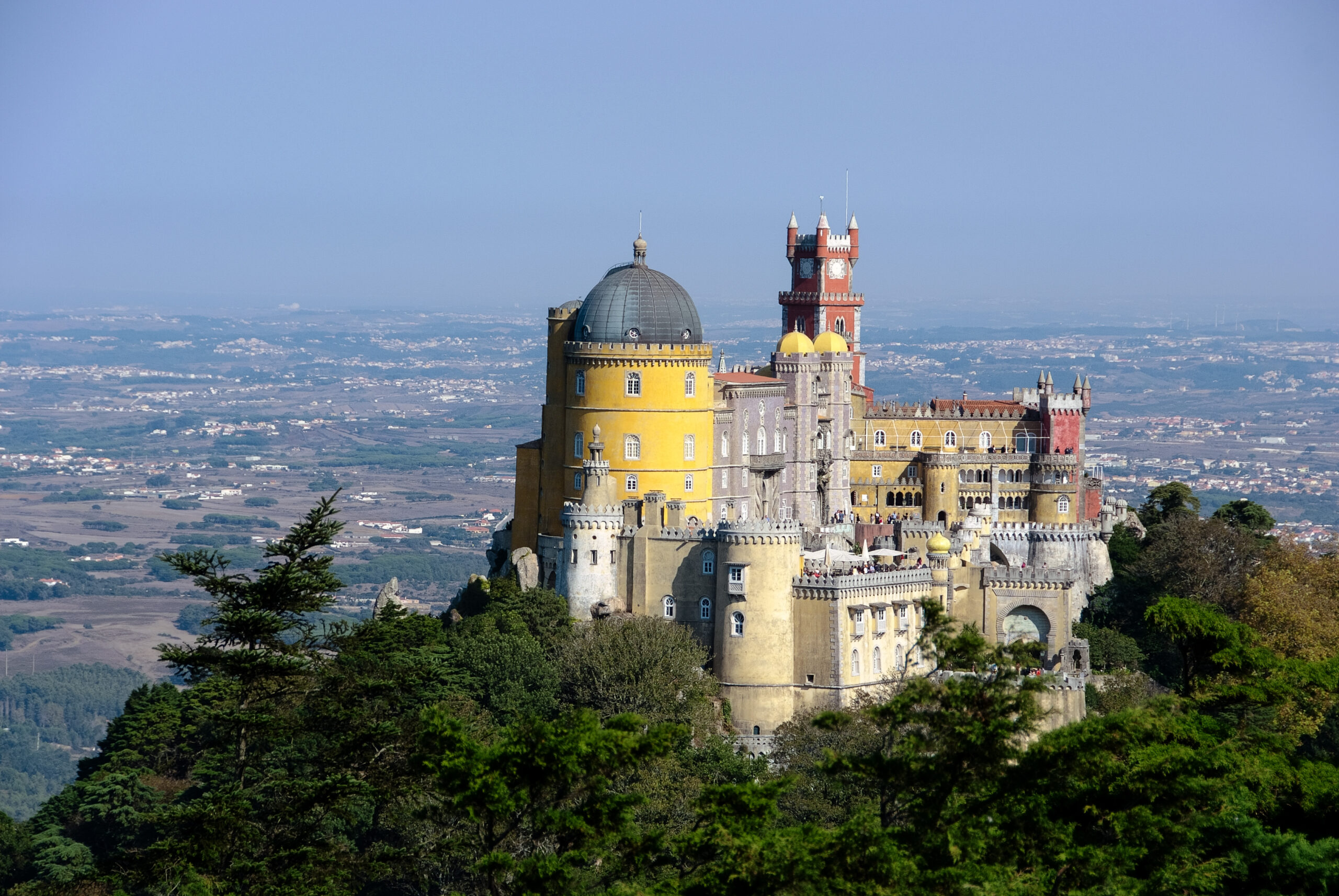 Red and yellow towers of Pena Palace rising above a wooded hillside in Sintra.