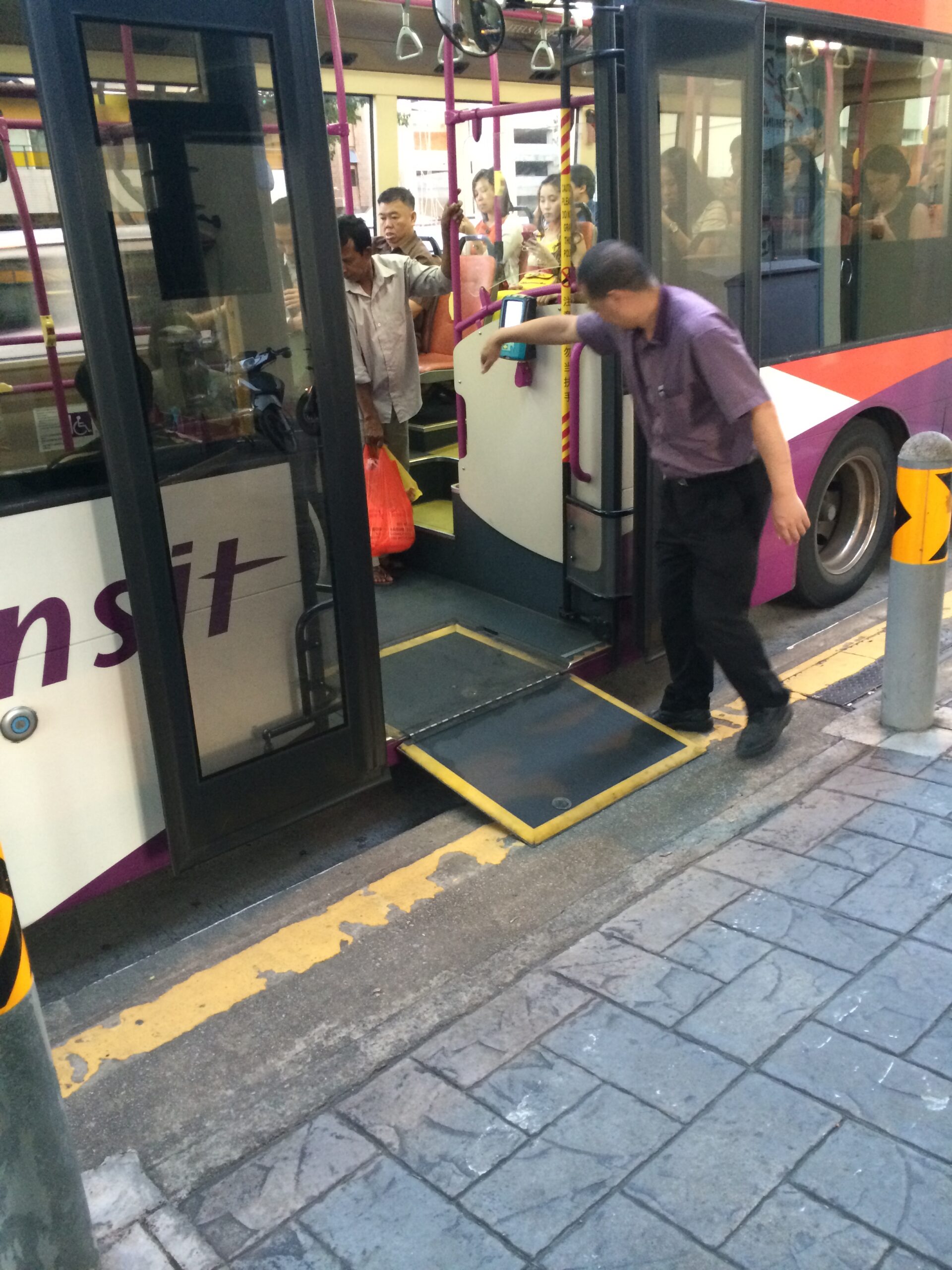 Bus boarding ramp extending from an open doorway toward the sidewalk, with a staff member beside it.
